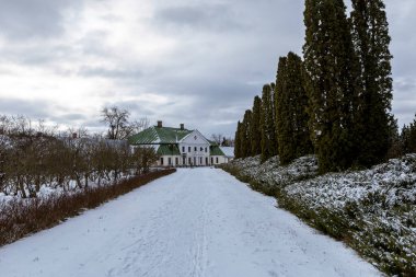 Karlı bir kış parkından geçerek ilerideki binaya doğru bir yürüyüş. Karla kaplı yollar, çıplak ağaçlar ve yumuşak gün ışığı sakin bir mevsimsel atmosfer yaratır..