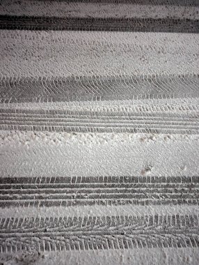 Lastik izleri, gece vakti yeni yağmış bir kardaki izler. Sokak lambaları buzlu yüzeyden yansıyarak sessiz, soğuk ve kasvetli bir kış manzarası yaratıyor..