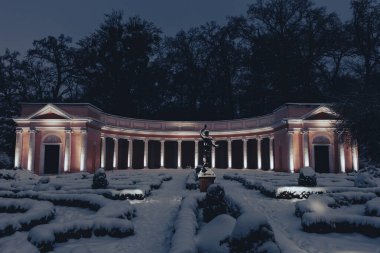 Akşamları karlı bir parkta sıcak ışıklarla aydınlatılan muhteşem bir klasik sütun. Altın parıltı, sütunlar ve yerdeki beyaz karla güzel bir tezat oluşturarak sofistike bir kış atmosferi yaratır.