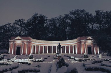 Akşamları karlı bir parkta sıcak ışıklarla aydınlatılan muhteşem bir klasik sütun. Altın parıltı, sütunlar ve yerdeki beyaz karla güzel bir tezat oluşturarak sofistike bir kış atmosferi yaratır.