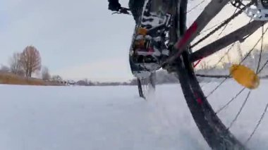 Donmuş bir göleti geçen bir bisikletin buz seviyesinden yakın çekim. Bu perspektif, sert lastikleri ve kışın kaygan, donmuş bir yüzey üzerinde dönen engebeli doğasını gösteriyor..
