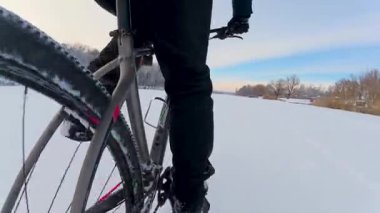 Kış bisikletinin yaratıcı alt görüntüsü. Bisiklet lastiği, açık bir kış gökyüzünün zeminine ve donmuş, karla kaplı bir göletin beyaz alanına karşı büyük ve güçlü görünür..