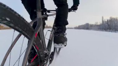 Donmuş bir gölette bisiklet sürmenin zemin katlı perspektifi. Kamera, buzun dokusunu ve soğuk mevsimsel bir macera sırasında tekerleğin ritmik hareketini yakalar..
