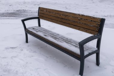 Buz gibi, karla kaplı bir park boş bir bankta sessiz bir kış parkında buz saçakları kenarlarında asılı duruyor. Buz, sessizlik ve soluk ışık soğuk, sakin bir kış durgunluğu atmosferi yaratır..