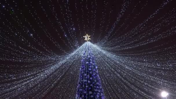 Υψηλή τεχνητό χριστουγεννιάτικο δέντρο με γιρλάντες στο δρόμο της πόλης — Αρχείο Βίντεο