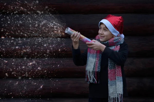 Yeni yıl cüce şapkalı neşeli genç bir adam havai fişeği patlattı. Kar ve kıvılcımlar uçuşuyor. koyu arkaplanda