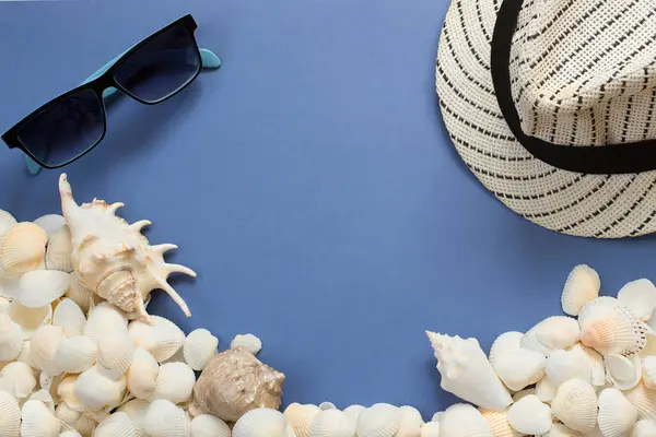 Top view of sunglasses, seashells, and a hat with copyspace. Summer concept. Light blue background.