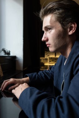 Masada oturan genç bir adamın portresi. Ceketli ve tişörtlü bir adam.