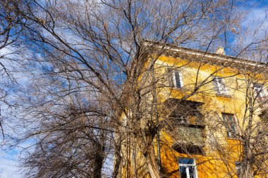 Sonbaharda ağaçların çıplak dalları ve mavi gökyüzüne karşı sarı büyük bir evin bir kısmı..