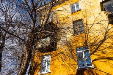 Sonbaharda ağaçların çıplak dalları ve mavi gökyüzüne karşı sarı büyük bir evin bir kısmı..