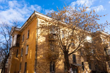 Sonbaharda ağaçların çıplak dalları ve mavi gökyüzüne karşı sarı büyük bir evin bir kısmı..