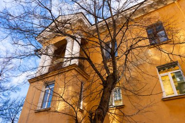 Sonbaharda ağaçların çıplak dalları ve mavi gökyüzüne karşı sarı büyük bir evin bir kısmı..