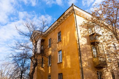 Sonbaharda ağaçların çıplak dalları ve mavi gökyüzüne karşı sarı büyük bir evin bir kısmı..