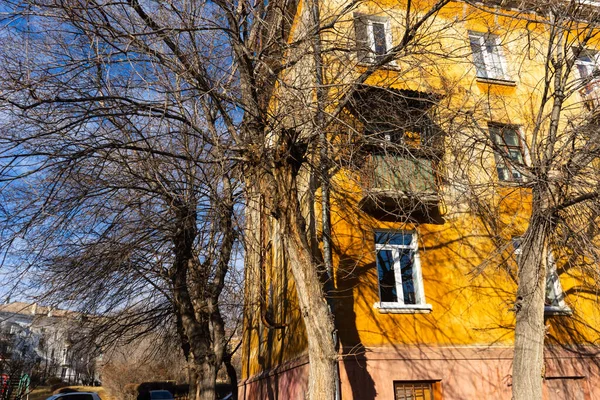 Sonbaharda ağaçların çıplak dalları ve mavi gökyüzüne karşı sarı büyük bir evin bir kısmı..