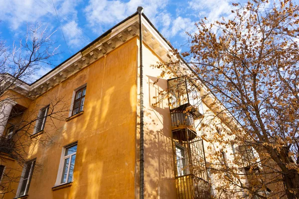 Sonbaharda ağaçların çıplak dalları ve mavi gökyüzüne karşı sarı büyük bir evin bir kısmı..