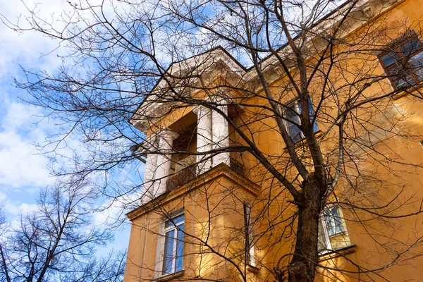 Sonbaharda ağaçların çıplak dalları ve mavi gökyüzüne karşı sarı büyük bir evin bir kısmı..