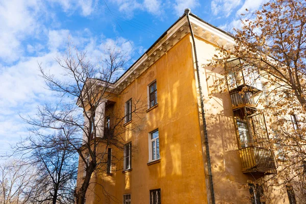 Sonbaharda ağaçların çıplak dalları ve mavi gökyüzüne karşı sarı büyük bir evin bir kısmı..