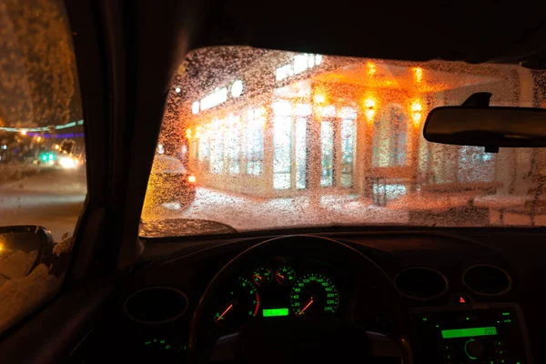 frosted car glass. snow covered car windshield. view from inside the car on the night city