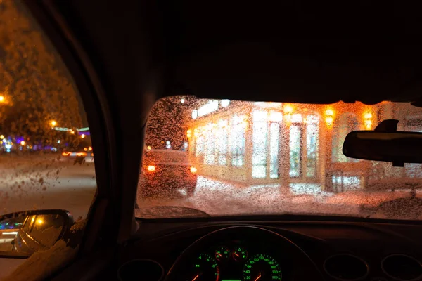 frosted car glass. snow covered car windshield. view from inside the car on the night city