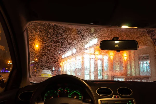 frosted car glass. snow covered car windshield. view from inside the car on the night city