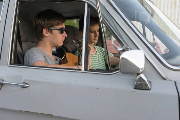 Two young man in the car. boy plays the guitar in the car. cheerful company of young people. journey together. fun pastime.