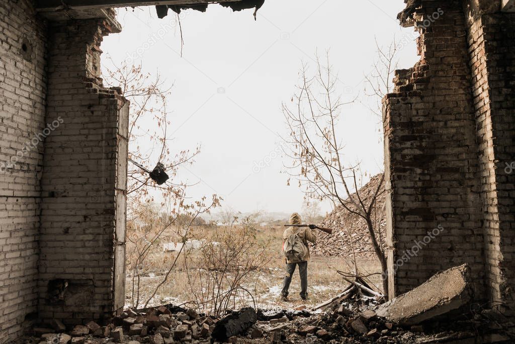 wandering boy. boy with a gun. boy goes to an abandoned building. boy stands in front of a building. Post apocalypse. Boy traveling on foot in a post-apocalyptic world in search of food.