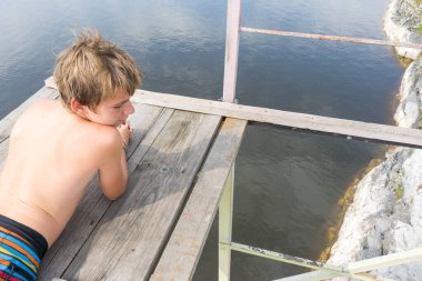 Çocuk suya atlamak için kulede dinleniyor. Çocuk göl kenarında dinleniyor. Şortlu bir yüzücü. Yaz tatili. Genç güneş banyosu. Yüksek irtifa korkusu