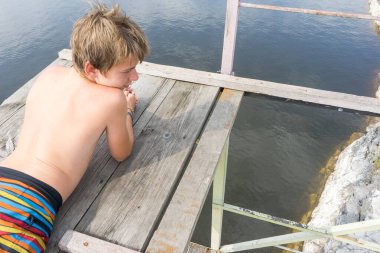 Çocuk suya atlamak için kulede dinleniyor. Çocuk göl kenarında dinleniyor. Şortlu bir yüzücü. Yaz tatili. Genç güneş banyosu. Yüksek irtifa korkusu