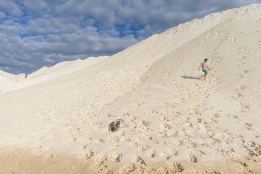 Sahilde duran çocuk uzaklığa bakıyor. Yüzme şortlu güneş gözlüklü genç bir adam. Çocuk çıplak. Gök mavisi denizin yanındaki beyaz kumdaki çocuk. mavi su.