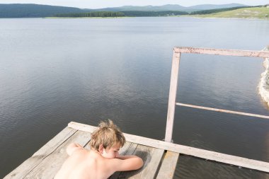 Çocuk suya atlamak için kulede dinleniyor. Çocuk göl kenarında dinleniyor. Şortlu bir yüzücü. Yaz tatili. Genç güneş banyosu. Yüksek irtifa korkusu