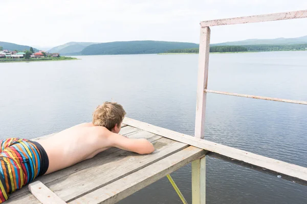 boy relaxes on a tower for jumping into water. Boy resting near the lake. Swimmer in shorts. summer rest. teenager sunbathe.  fear of high altitude