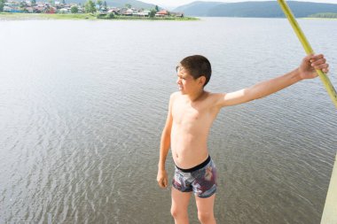 Çocuk suya atlamak için kulede dinleniyor. Çocuk göl kenarında dinleniyor. Şortlu bir yüzücü. Yaz tatili. Genç güneş banyosu. Büyük bir yükseklikten suya atlamak. Yüksek irtifa korkusu