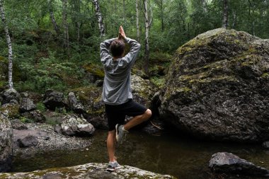 Genç adam ormanda duruyor. Arkadan bak. Açık havada yoga egzersizleri.