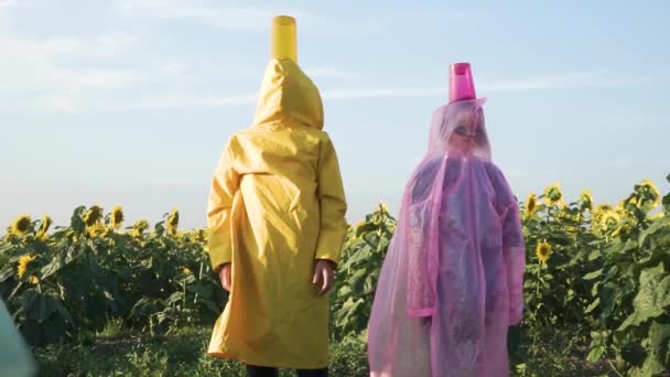 ひまわり畑を背景に黄色とピンクのレインコートを着た男と女の2人 明るい色 アートビデオ — ストック動画