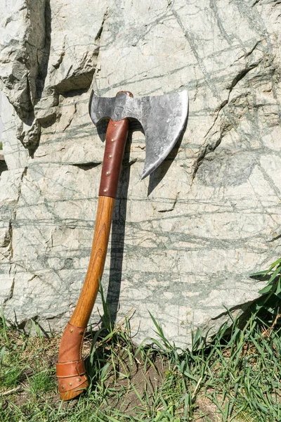 the battle ax is on the ground next to a large stone. forged ax