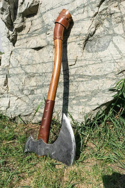 the battle ax is on the ground next to a large stone. forged ax