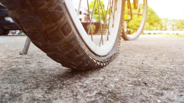 Eski bisikletin arka lastiği otoparkta patlamış. Birinin tamir etmesini bekliyormuş. Akşamları güneş ışığı ve gelişmiş renklerle düzenlenmiş.