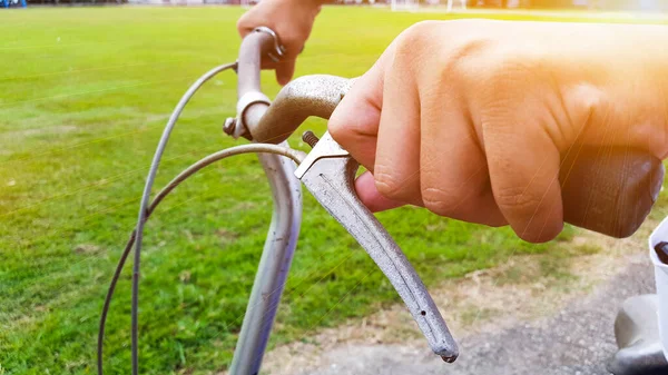 Hands are on a vintage bike handle which the break shaft tip is broken, the handle is at closed to the green field, the sunlight shines on a hand