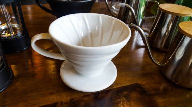 Beyaz çömlekçi kahve fincanı mermer ahşap zeminde cam ve gümüş renkli çaydanlıklarla çevrili.