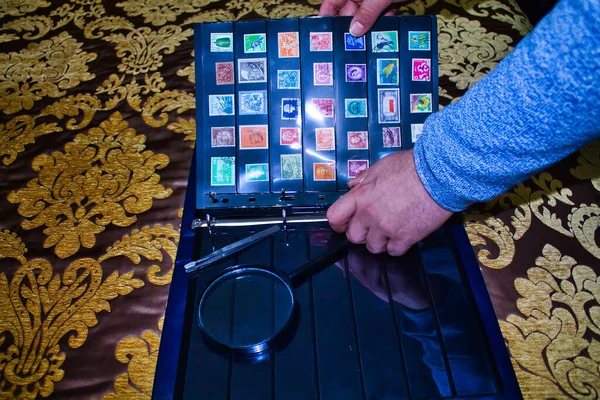 Büyüteçli ve cımbızlı bir adam dünyanın dört bir yanından farklı pullara bakıyor.