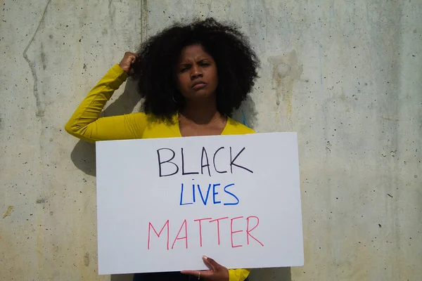 angry african-american woman with raised fist holds up a banner reading black lives matter