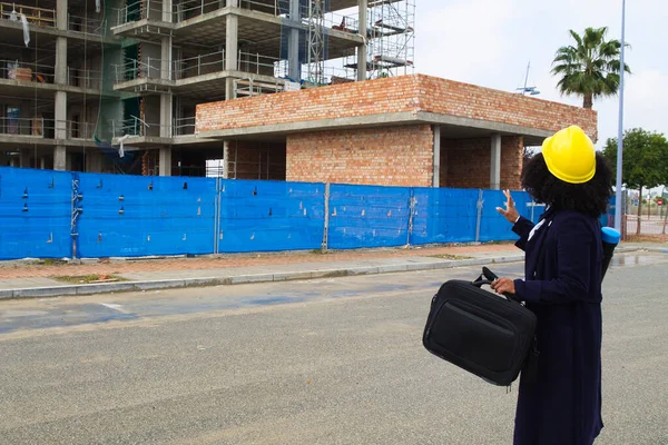 african-american woman construction manager in yellow hardhat set out to check the construction of the flats. The architect holds a briefcase black in her hand.