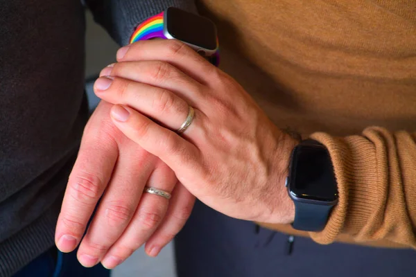 Detail of hands of homosexual couple showing their wedding rings after having said I DO. You can see detail of the gay pride flag on the watch
