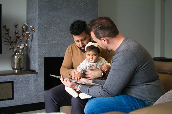 Eşcinsel çift ve kızları kanepede oturmuş küçük kızlarına masal okuyorlar..