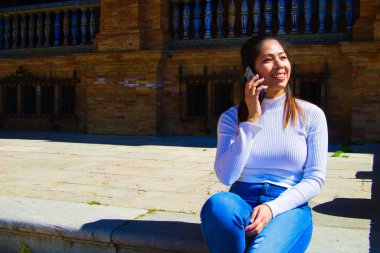 Güzel genç Asyalı turist. O, cep telefonuyla konuşurken bir meydanın merdivenlerinde dinleniyor.