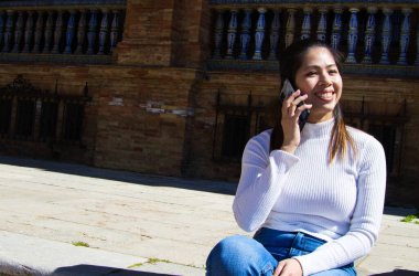 Güzel genç Asyalı turist. O, cep telefonuyla konuşurken bir meydanın merdivenlerinde dinleniyor.