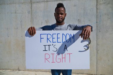 Afro-Amerikalı bir adam elinde özgürlüğün bir hak olduğunu gösteren bir pankart tutuyor. Adamın sol elinde kelepçe ya da kelepçe var. İnsan hakları. Irkçılığı bırak. Siyah hayatlar önemlidir..