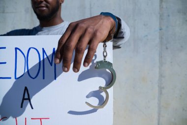 Afro-Amerikalı bir adam elinde özgürlüğün bir hak olduğunu gösteren bir pankart tutuyor. Adamın sol elinde kelepçe ya da kelepçe var. İnsan hakları. Irkçılığı bırak. Siyah hayatlar önemlidir..