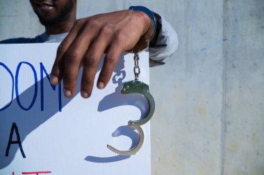 Afro-Amerikalı bir adam elinde özgürlüğün bir hak olduğunu gösteren bir pankart tutuyor. Adamın sol elinde kelepçe ya da kelepçe var. İnsan hakları. Irkçılığı bırak. Siyah hayatlar önemlidir..