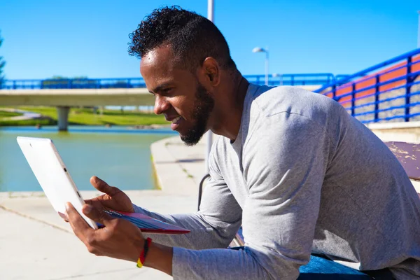 Parkta çalışan Afro-Amerikalı bir adam. Adam dikkatle bilgisayar ekranına bakıyor. Gözlerinin bilgisayar ekranına baktığını görebilirsiniz.